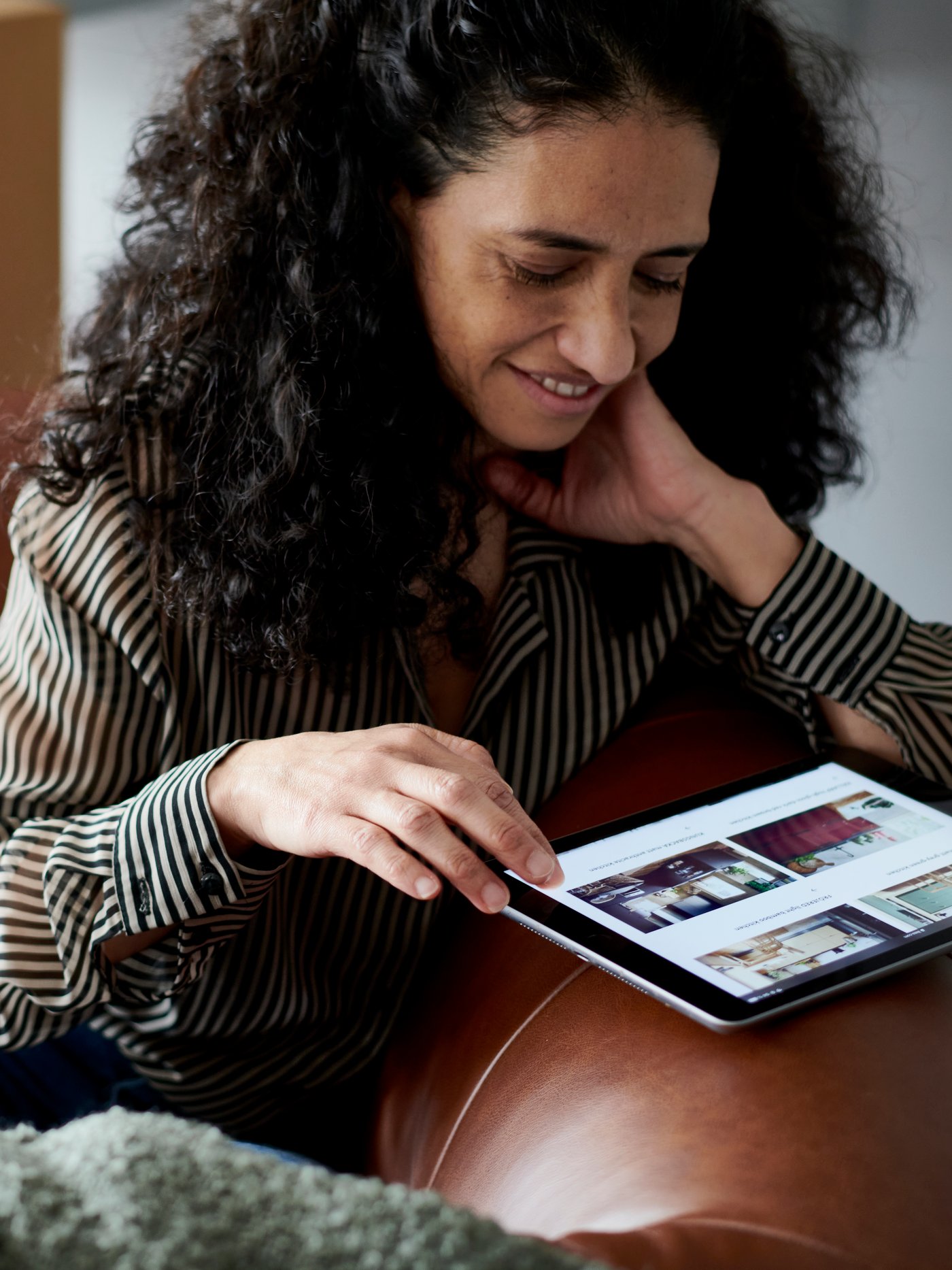 Woman browsing the IKEA website on a tablet while sitting on a brown leather sofa