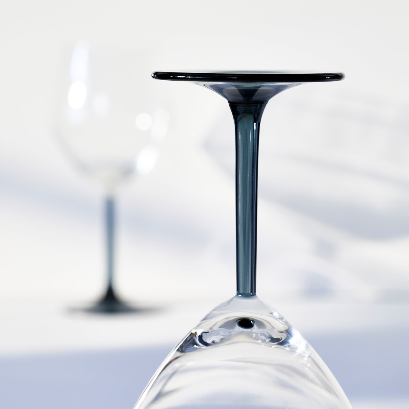 A closeup of the grey stem of a RÖDRÄKA wine glass, which is standing upside down on a bright surface.