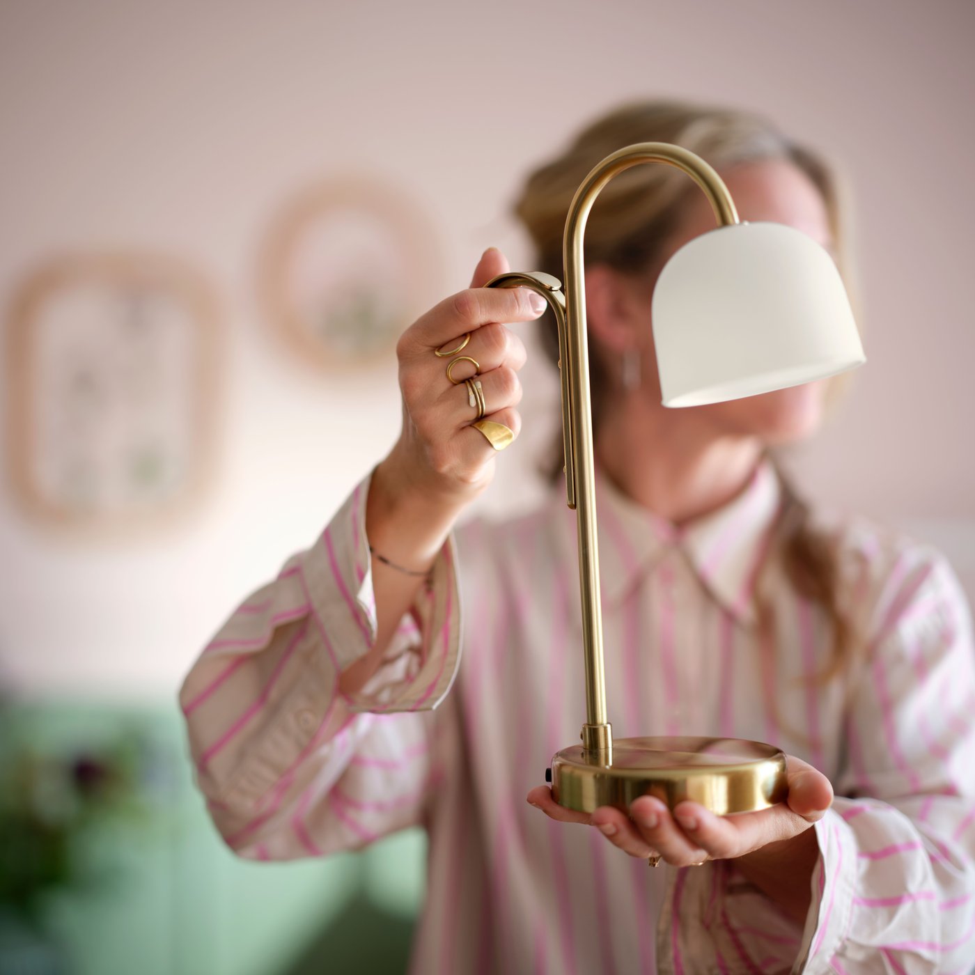 Henkilö pitelee paristokäyttöistä messingin väristä TVÅMASTAD-led-valaisinta, jossa on lasikupu.