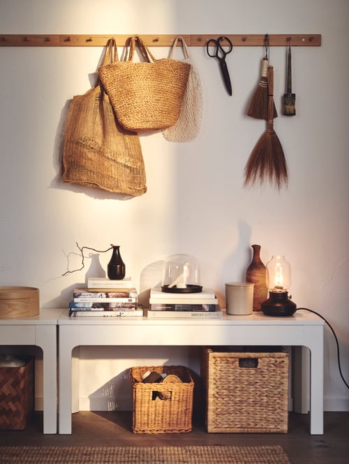 Hallway area with two brown racks with six knobs on which are bags and a pair of scissors. Under the rack are two benches.