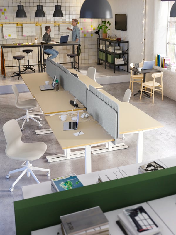 Sala de reuniões com uma mesa grande e várias cadeiras à volta, uma planta na janela e um homem a trabalhar no computador.