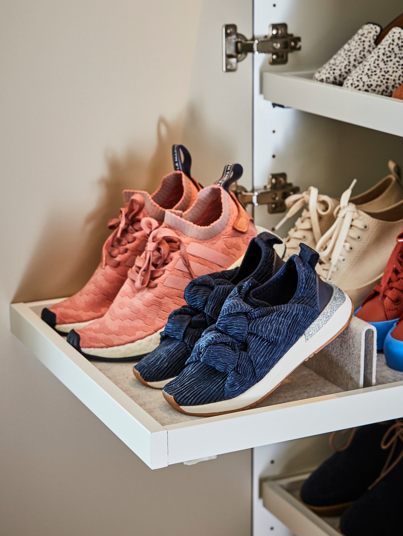 Num roupeiro PAX, um tabuleiro extraível com sapateira KOMPLEMENT em branco com quatro pares de ténis de diferentes cores.