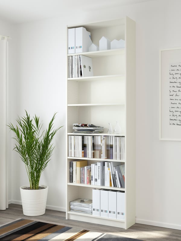 Ein weißes BILLY Bücherregal  80 breit, 28 tief und 237 cm hoch, steht vor einer weißen Wand. Daneben steht eine Zimmerpflanze. 