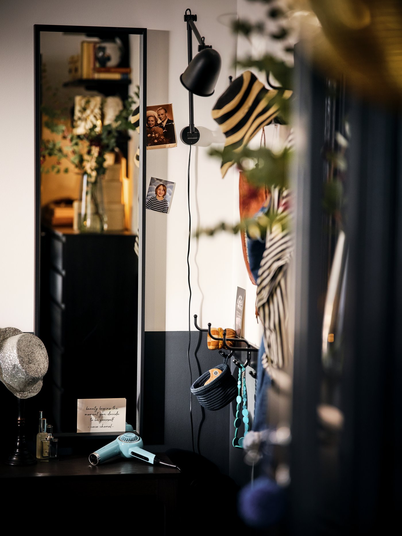 A corner of a room with a black NISSEDAL mirror and a wall-mounted, black SKURUP lamp amid various decorative items.