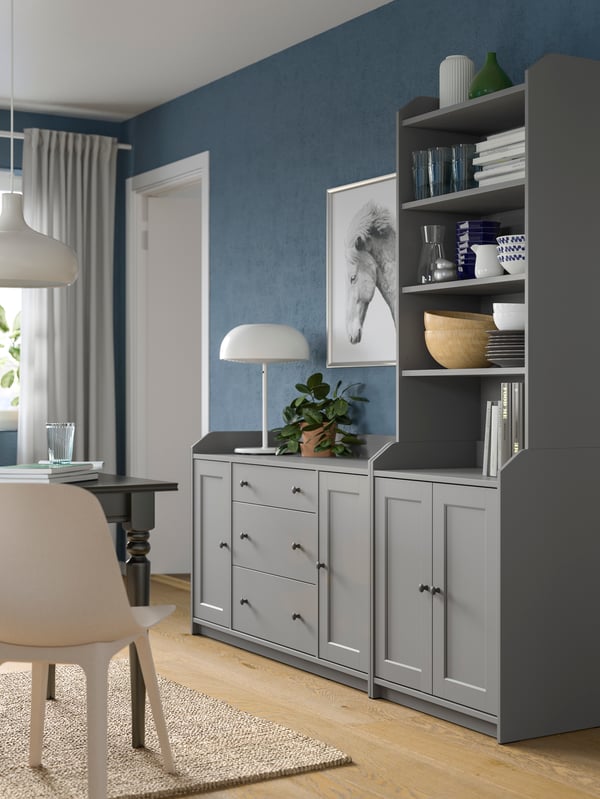 A grey HAUGA combination of a chest of drawers side by side with a high cabinet, standing by a living-room wall.