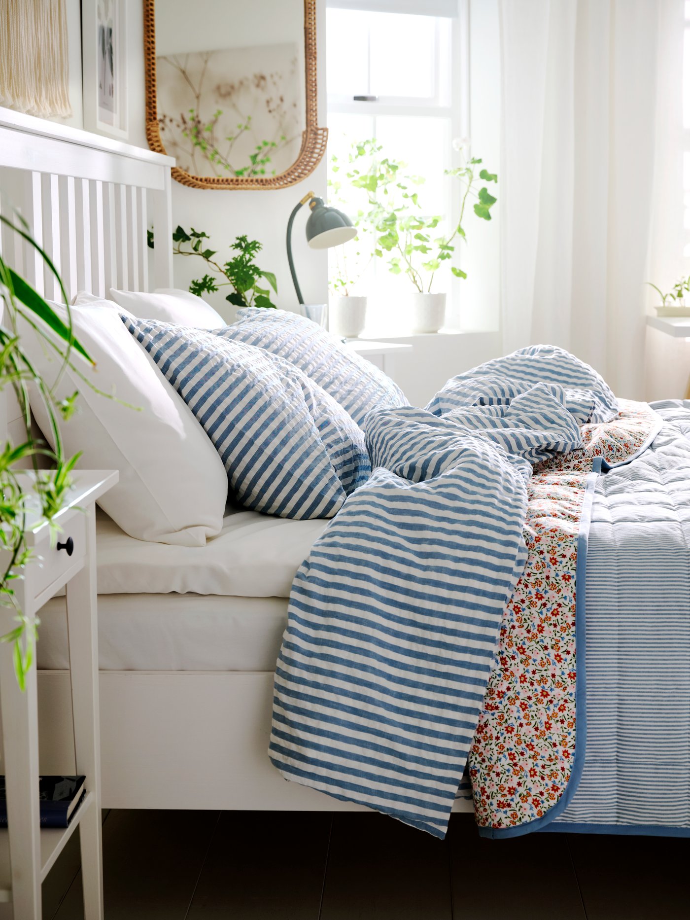 HEMNES bed seen from the side with windows and white curtains in the background. Bedding in light blue, white and pink.