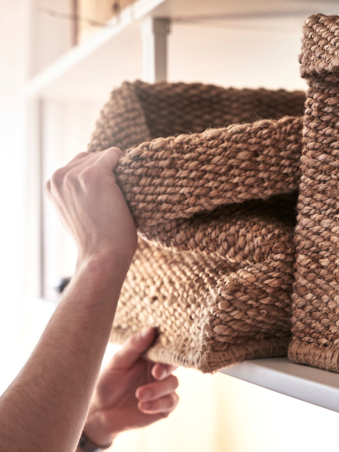 En person plockar ner en flätad förvaringskorg från en vägghylla.