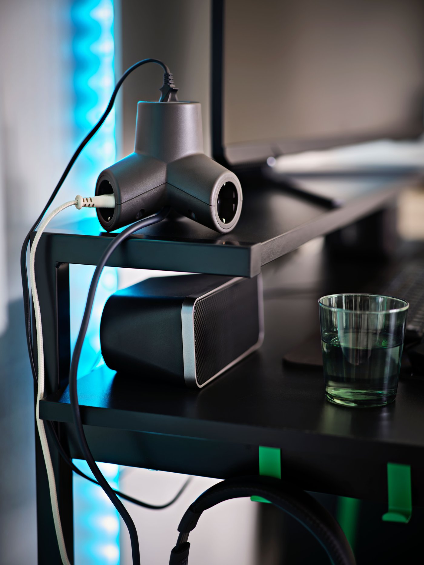 Ein dunkelgraues, 4-fach HORNFELS Verlängerungskabel mit dreibeiniger Form, das auf dem Monitorregal eines dunkel gefärbten Gaming-Schreibtisches liegt.