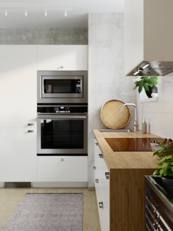 The side view of a bamboo veneer HOLMARED custom made worktop framing white cabinets in an airy and light, L-shaped kitchen.