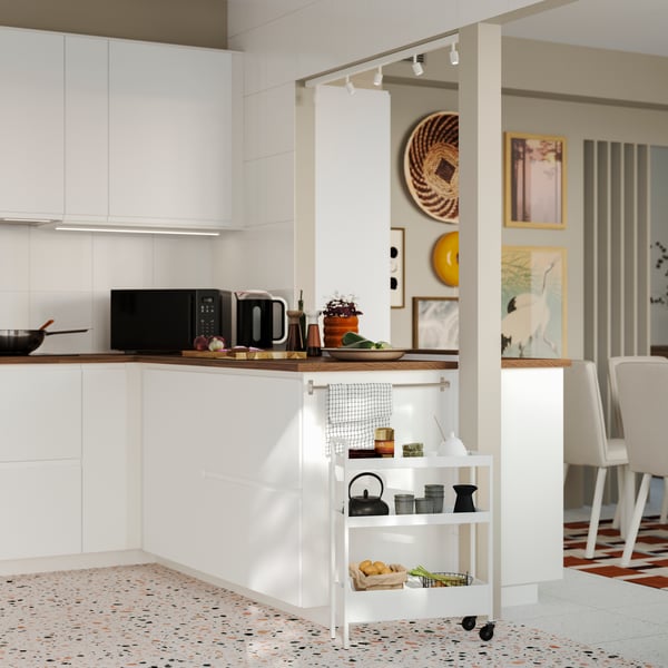 A peninsula made of METOD kitchen cabinets has white VOXTORP fronts and there’s a dining room in the background.