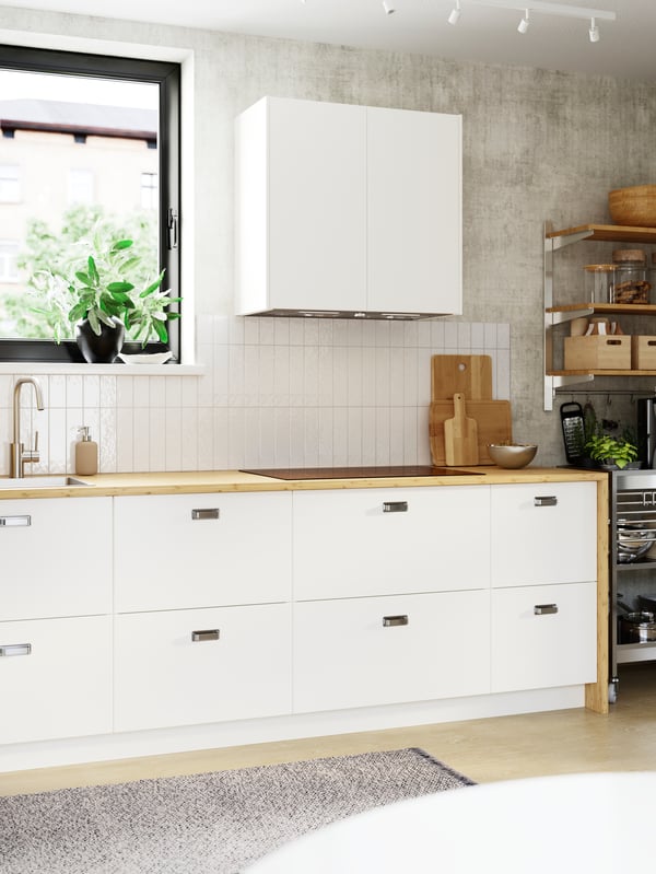 A bright, white-tiled kitchen wall has two high cabinets and eight spacious drawers with smooth, white VEDDINGE fronts.