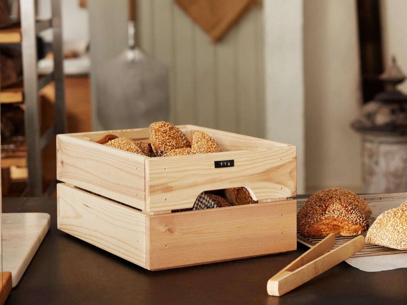 A pine KNAGGLIG box sits filled with bread on a kitchen counter. 