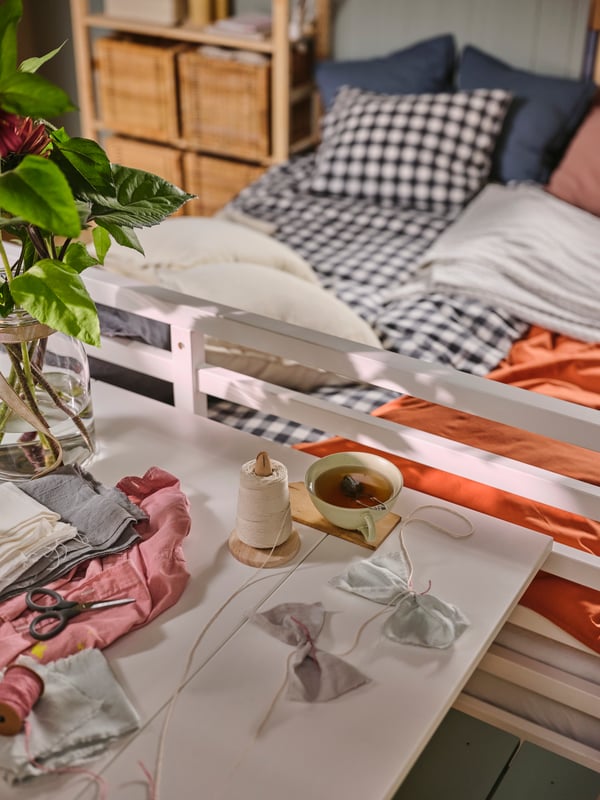 Ein weisser HAUGA Klapptisch steht am Fussende eines TARVA Bettgestells. Das Bett ist mit Bettzeug in EKTANDVINGE Bettwäsche mit einem Karomuster in Anthrazit und Weiss bezogen.