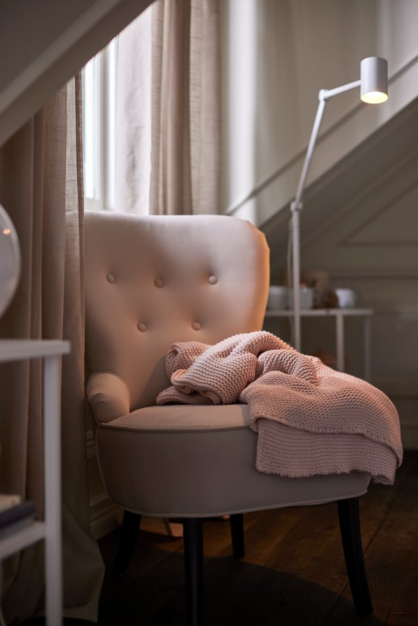 Un sillón beige REMSTA en el costado de un dormitorio con una manta sobre el asiento.