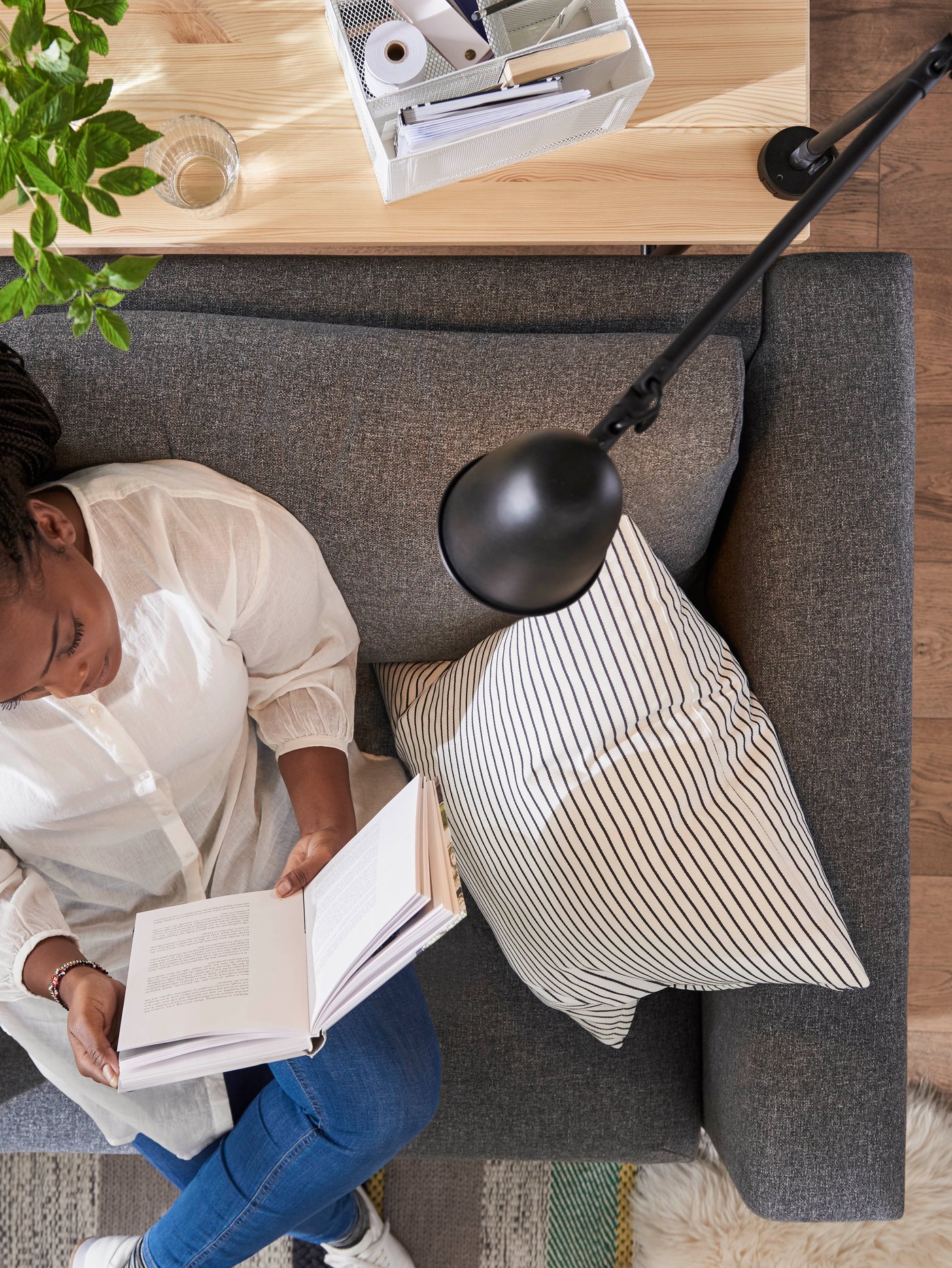 Una mujer sentada en un sillón de la serie VIMLE sosteniendo un libro, con una lampara de pie de la serie SKURUP sobre ella.