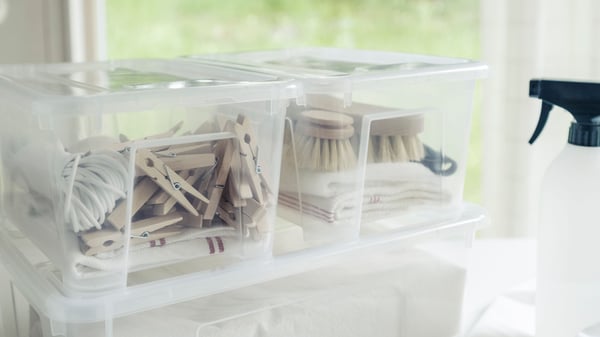 Eine SAMLA Box mit Deckel, darin sind Wäschklammern und Putzzeug.