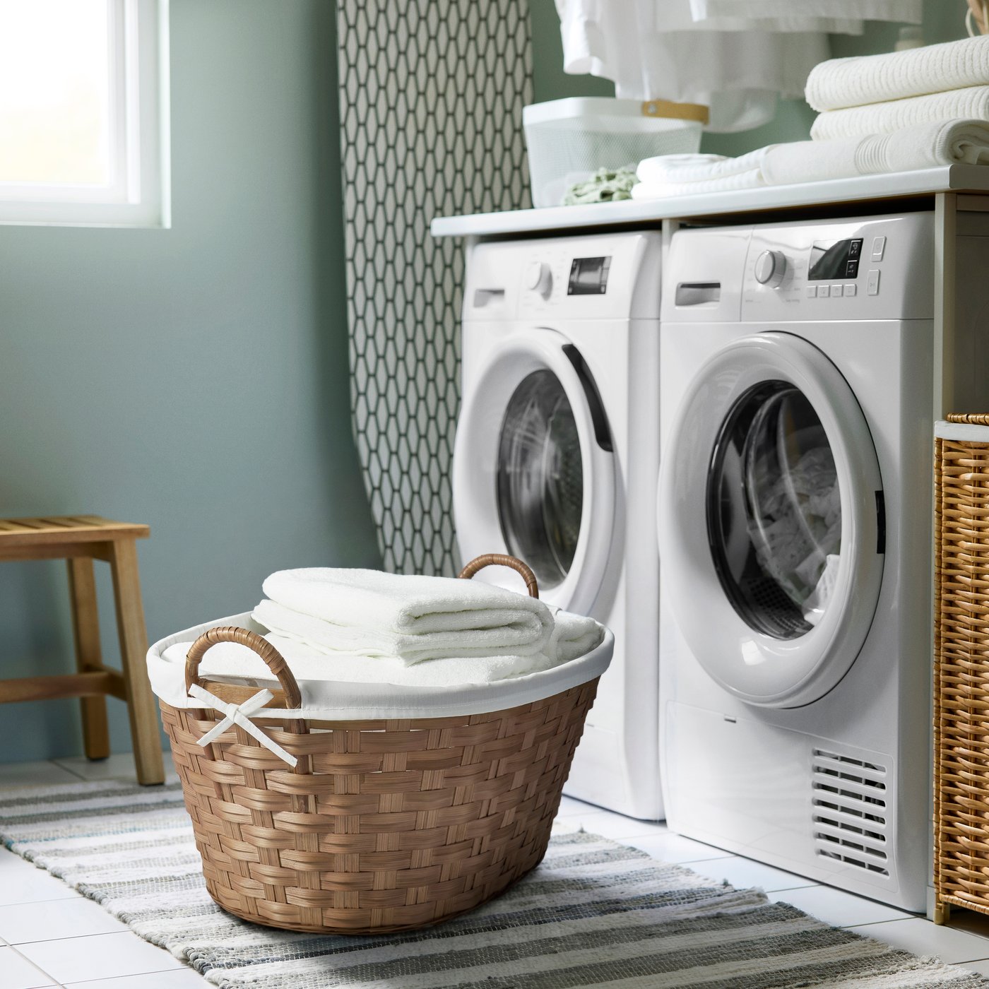 A laundry room with a laundry basket in the foreground, filled with white towels, in front of a washing machine and dryer.