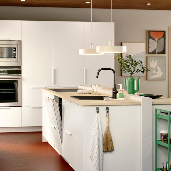 A white VEDDINGE kitchen with an island, FLÅBODA dishwasher, VASKARBO convection wall oven in stainless steel, lamps hanging.