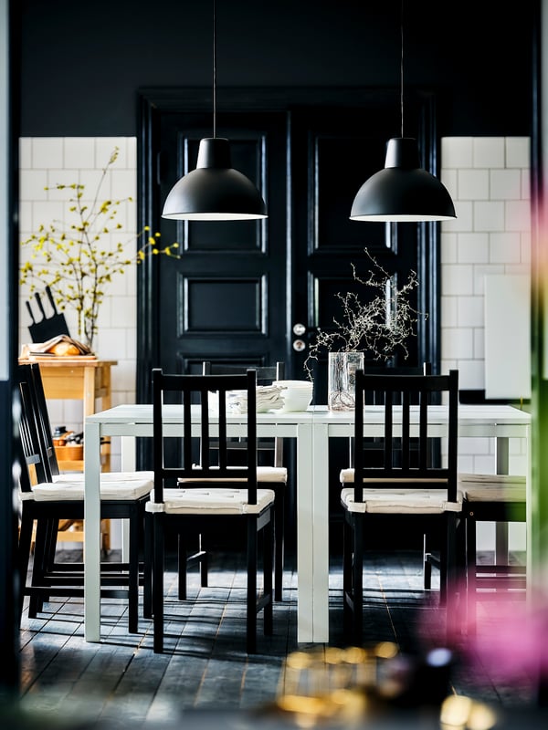 Three IKEA ÖSTANÖ dining chairs in a red-brown colour in front of a foldable white wall dining table.