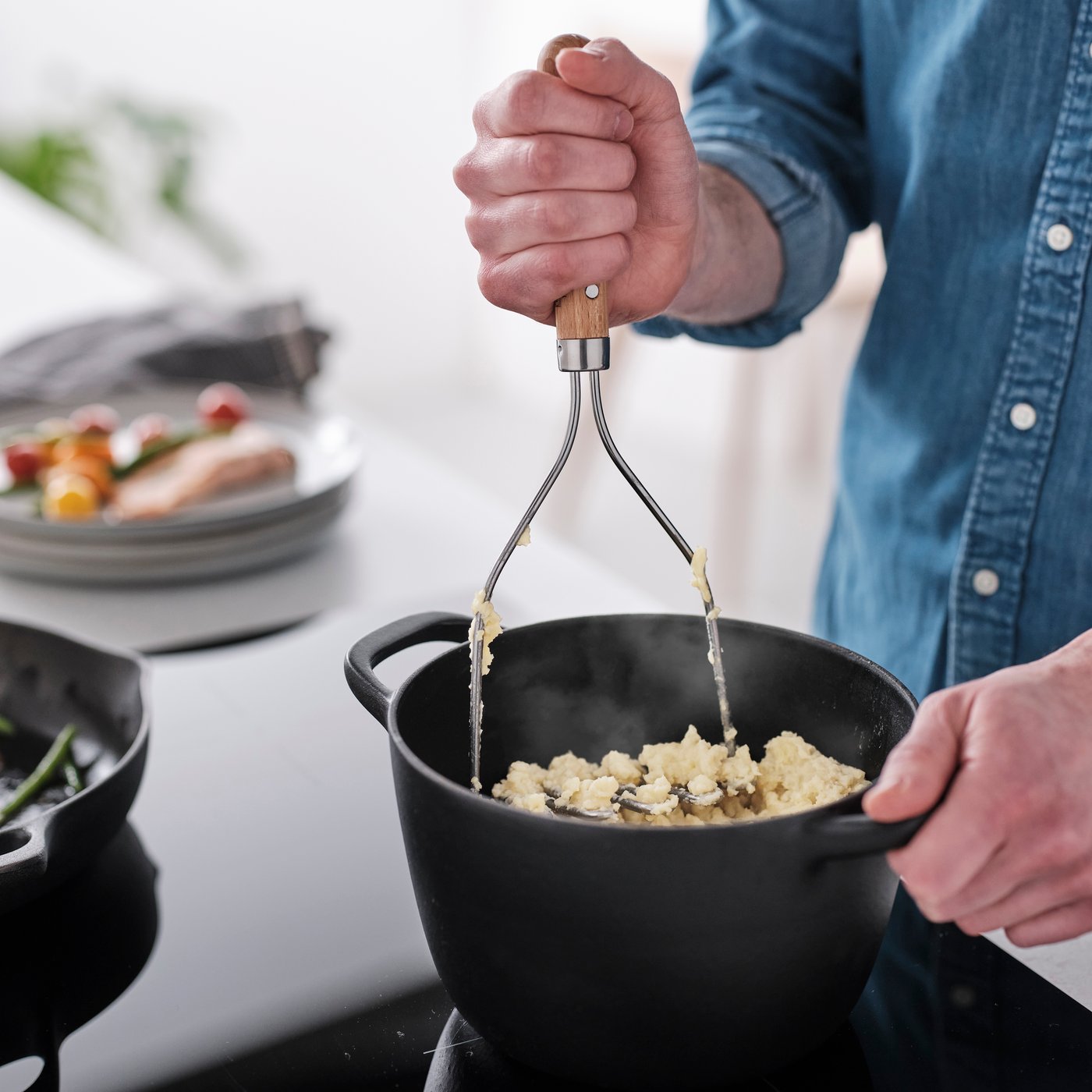 En hånd holder en VARDAGEN kartoffelpresser og moser kogte kartofler i en gryde.