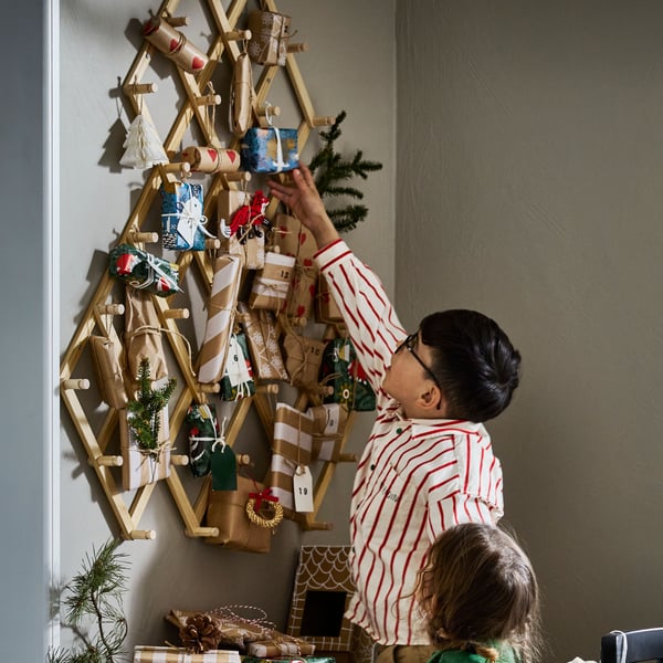 Barn utforskar en VINTERFINT väggdekoration fylld med små inslagna paket och julprydnader, som liknar en adventskalender.
