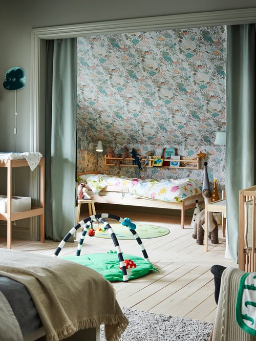 Bedroom with a beige changing table, a blue baby gym, and a beige bed frame with slatted base with a white duvet set.