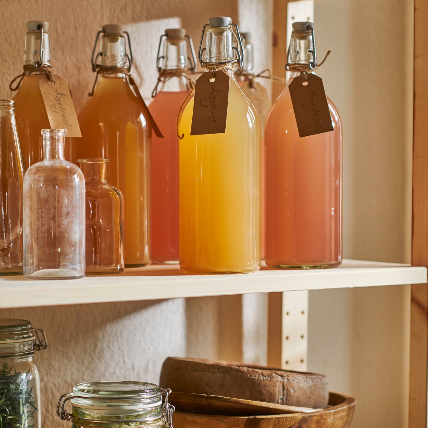 A shelf with KORKEN bottles with labels tied around the bottle necks, next to some empty decorative bottles.