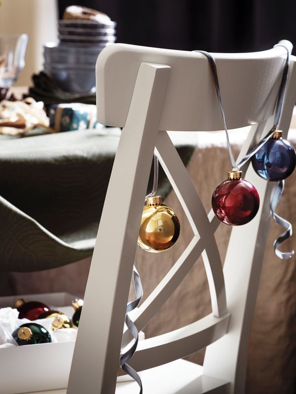 Sedia bianca in legno in stile tradizionale, vicino a un tavolo da pranzo, decorata con palline colorate dai toni vivaci - IKEA