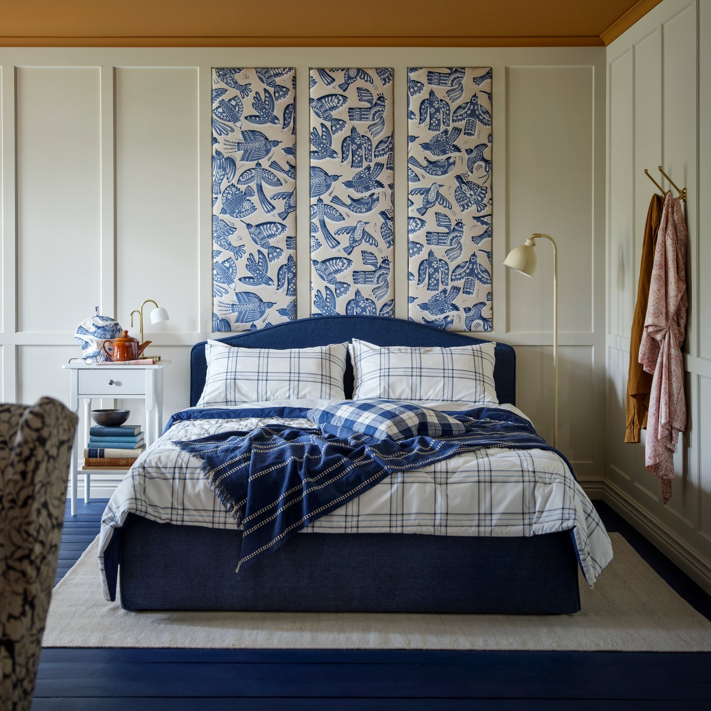 Et blått og hvitt LINSNÄRJA dynesett er arrangert på en RAMNEFJÄLL polstret sengestamme, med puter og et pledd.