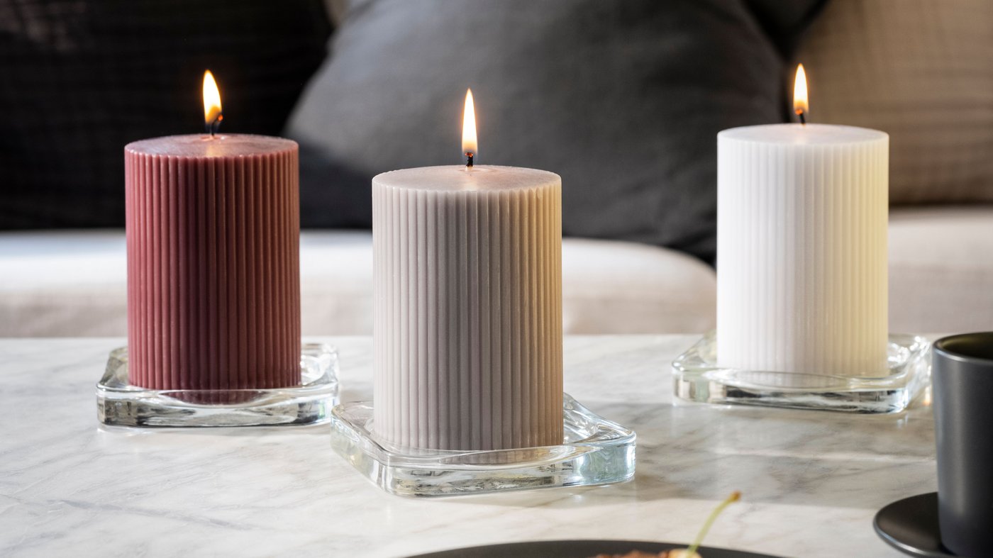 Eetruimte in Scandinavische stijl met brandende KOPPARLÖNN geurkaarsen en theelichtjes op een eettafel bij een groot raam.