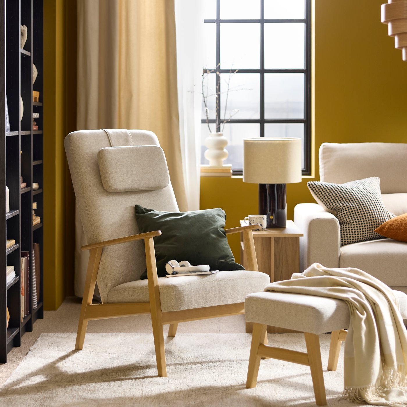 A bright living room with a light-beige EKENÄSET high-back armchair and footstool flanked by a HOLMERUD coffee table.