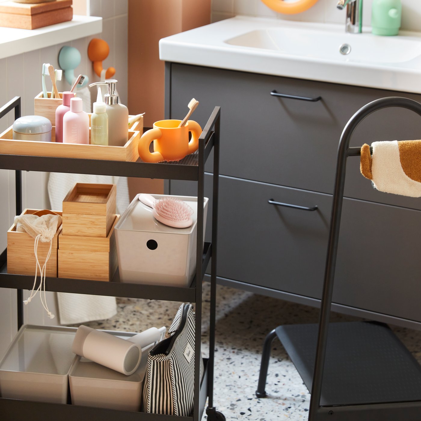 Tiled bathroom setting with a black NISSAFORS trolley with storage boxes, accessories, toiletries, next to a step stool.