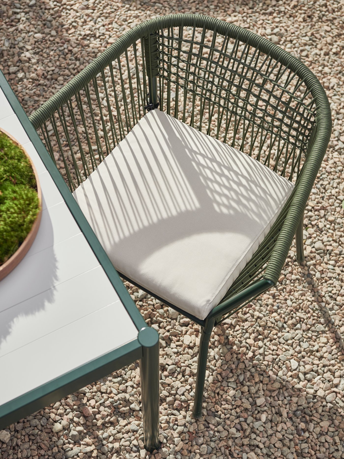 A dark-green SEGERÖN chair with armrests by a dark-green-and-light-grey SEGERÖN table, both standing on sunlit gravel.