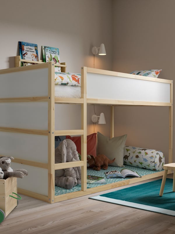Una cama para niños KURA de IKEA con una zona de juegos en la parte inferior del camarote que tiene una alfombra y cojines.