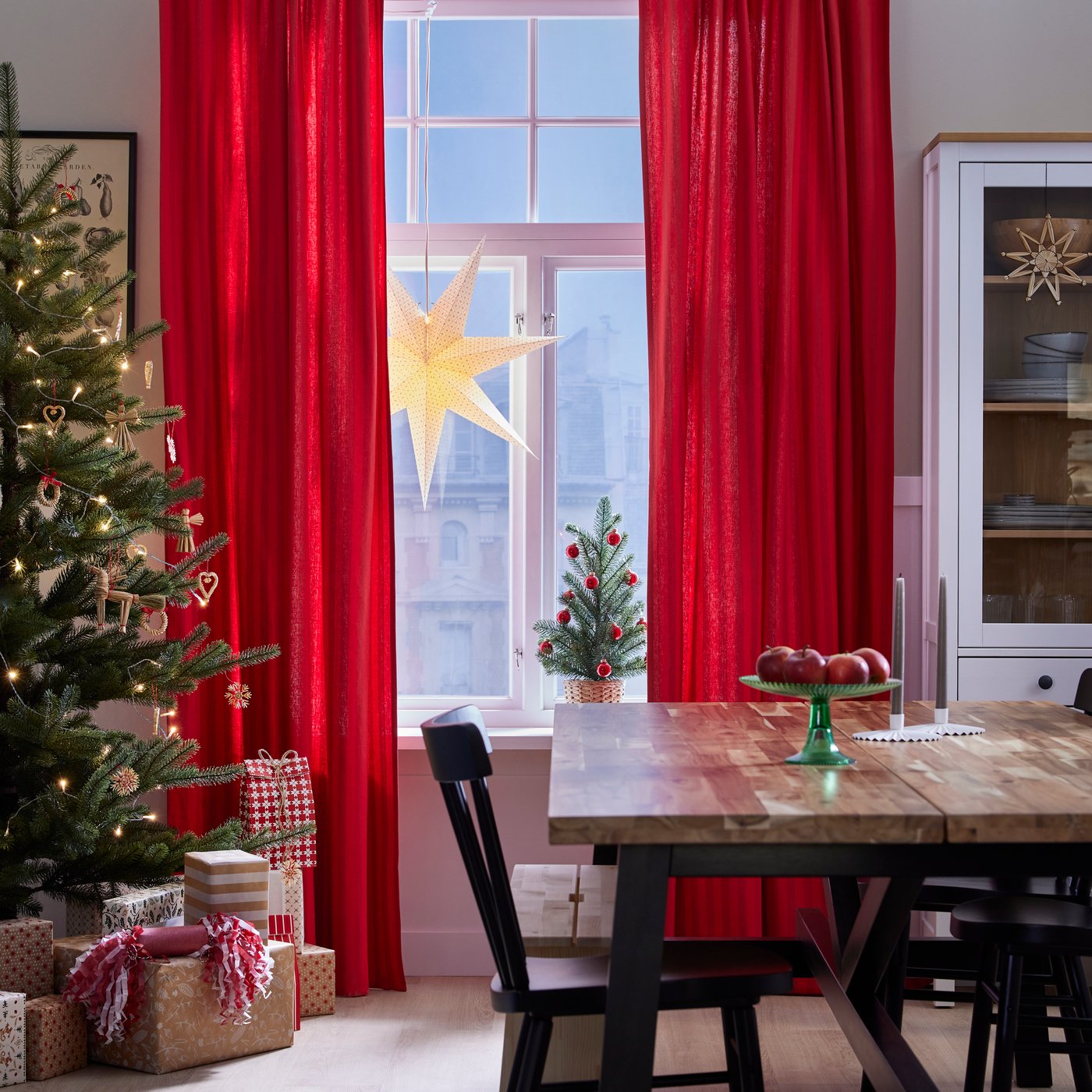 Foto de comedor decorada con cortinas rojas, luces amarillas y un árbol de navidad con regalos debajo.
