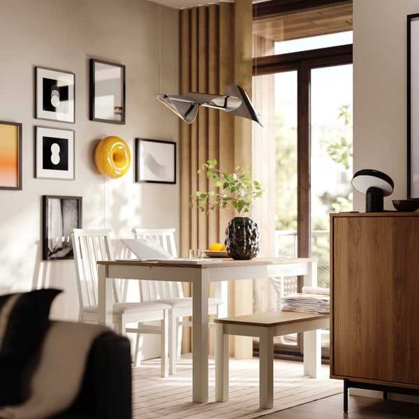 Le coin repas est équipé d'une table extensible ÅLHULT beige/marron avec un banc d'un côté et deux chaises à assise souple de l'autre.