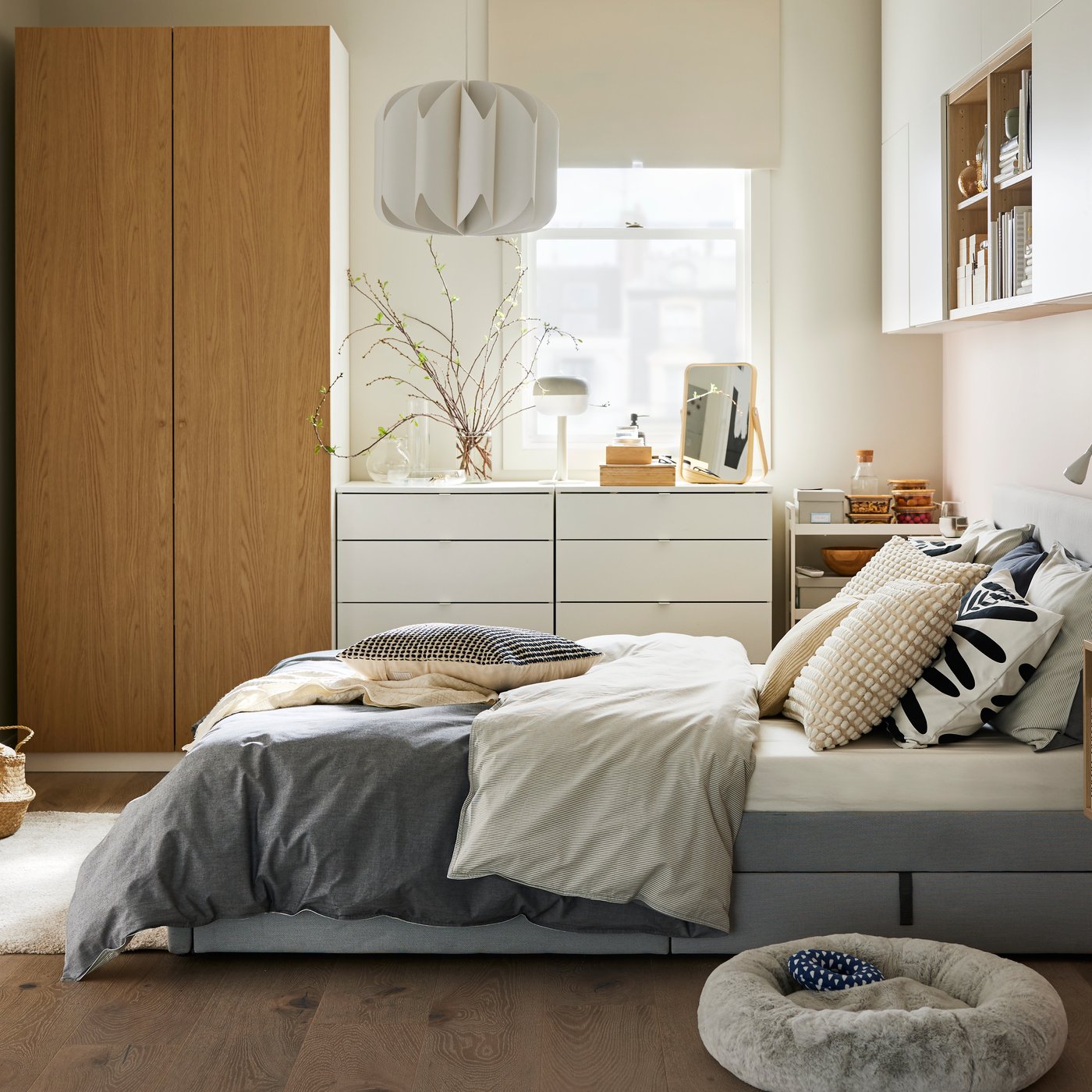 A GLADSTAD bed with BLÅVINDA bed linen on it, by a white/oak effect PAX/STORKLINTA wardobe and two white chests of drawers.