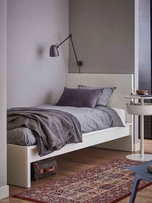 Cadre de lit haut MALM blanc couvert d’une housse de couette grise et d’un plaid gris foncé dans une pièce aux murs gris avec une applique gris foncé.