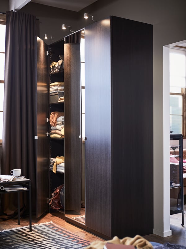 A PAX wardrobe system with one door open revealing folded clothing on shelves inside.