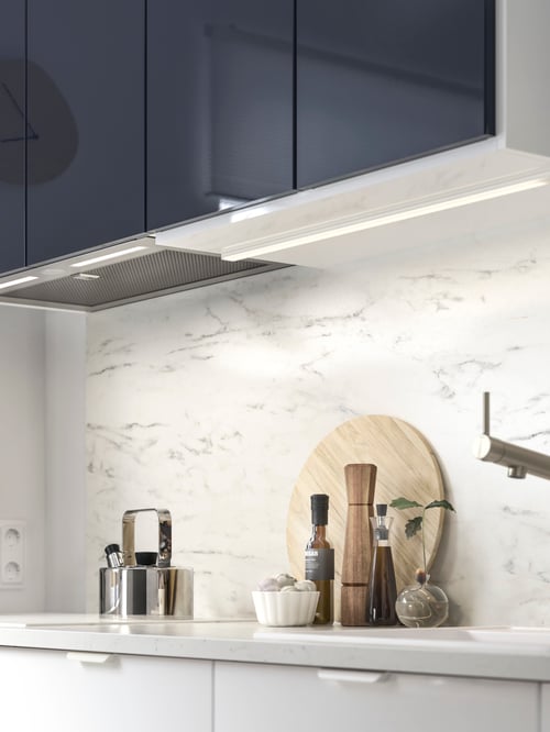 UNDERVERK kitchen hood is integrated under black-blue cabinets with lit halogen bulbs above a marble effect worktop.