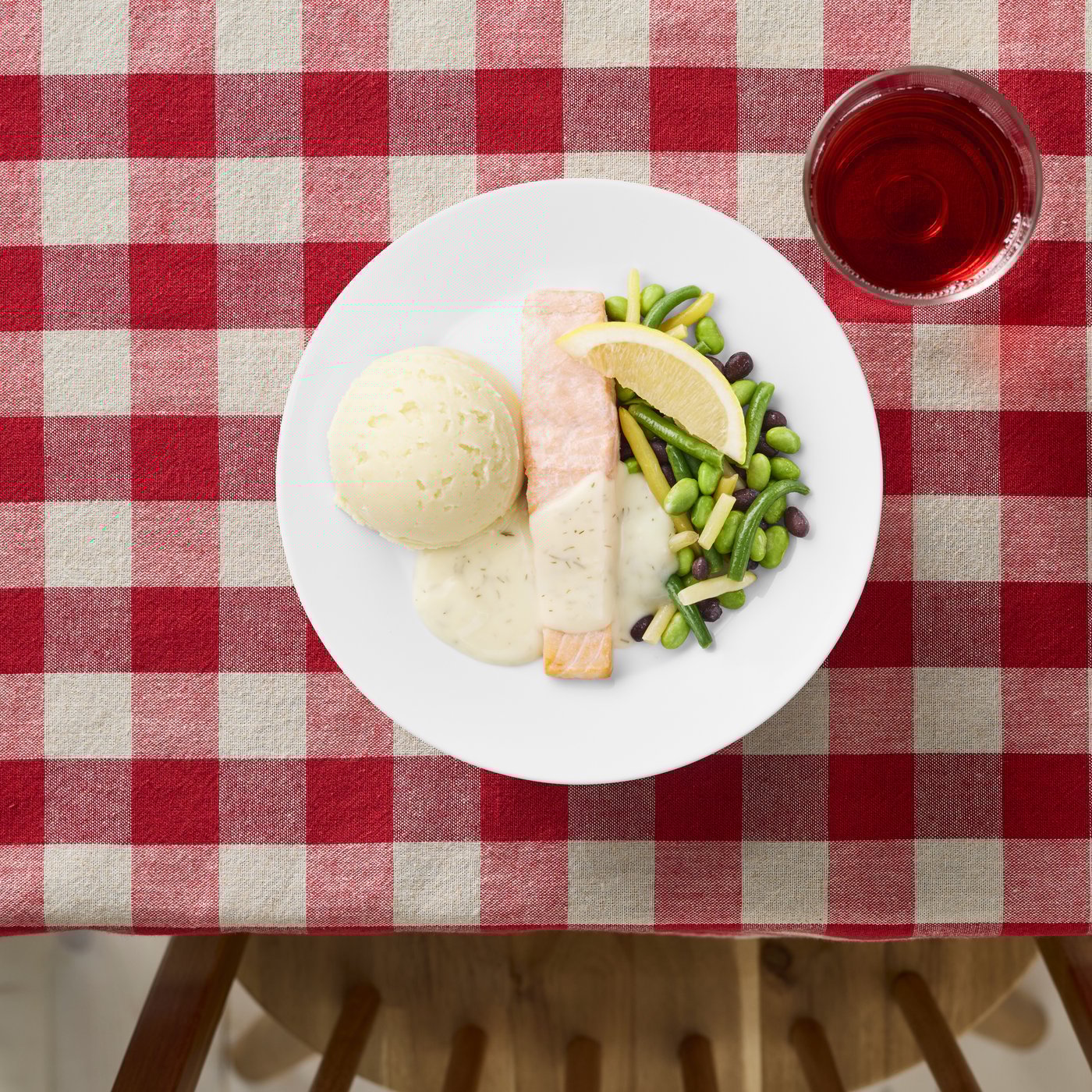 Danie główne z łososiem na białym talerzu, usytuowany na stole pokrytym obrusem w biało czerowną kratę.