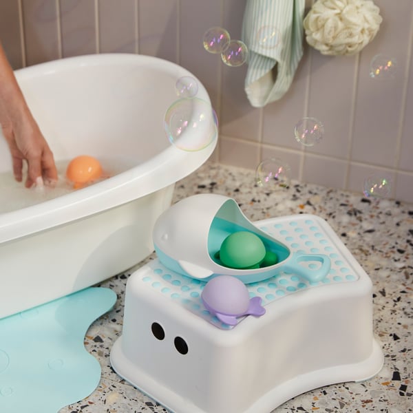 An adult’s hand swishes water in a LÄTTSAM baby bath with an ÄNGSHUMLA bath toy in it. The other toys are outside the bath.