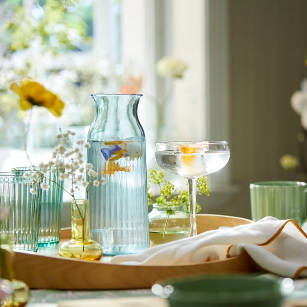 Svetlotirkizni SMÖRFISK karaf okružen je ukrasnim vazama i elegantnim staklenim posuđem na stolu.