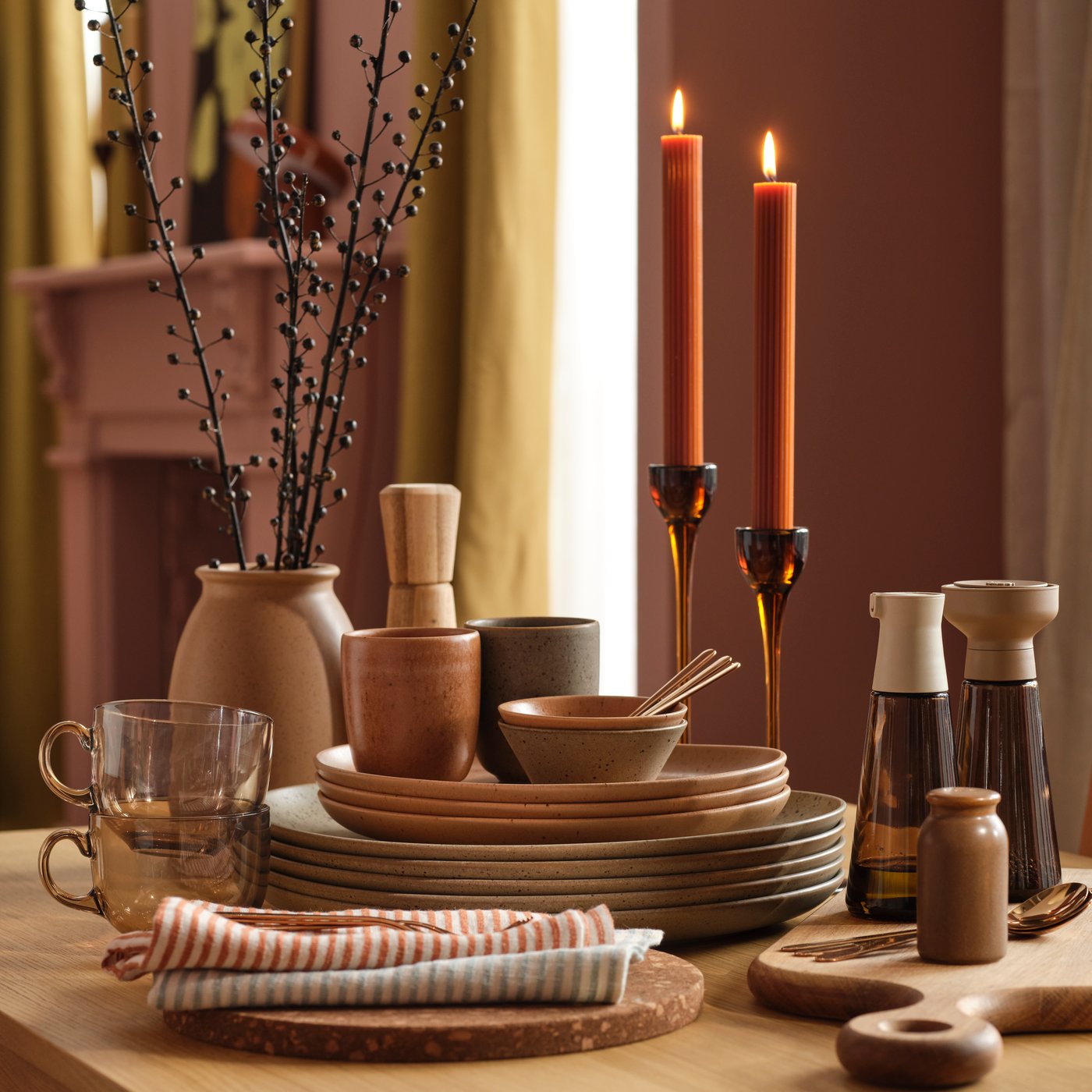 GRÅRÄV serveware are stacked with other dishes on a dining table along with lit candles in a pink dining room.