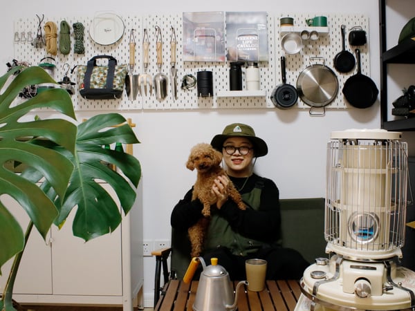 Doris and her pet dog posing with her camping gear that’s stacked up on a wall.