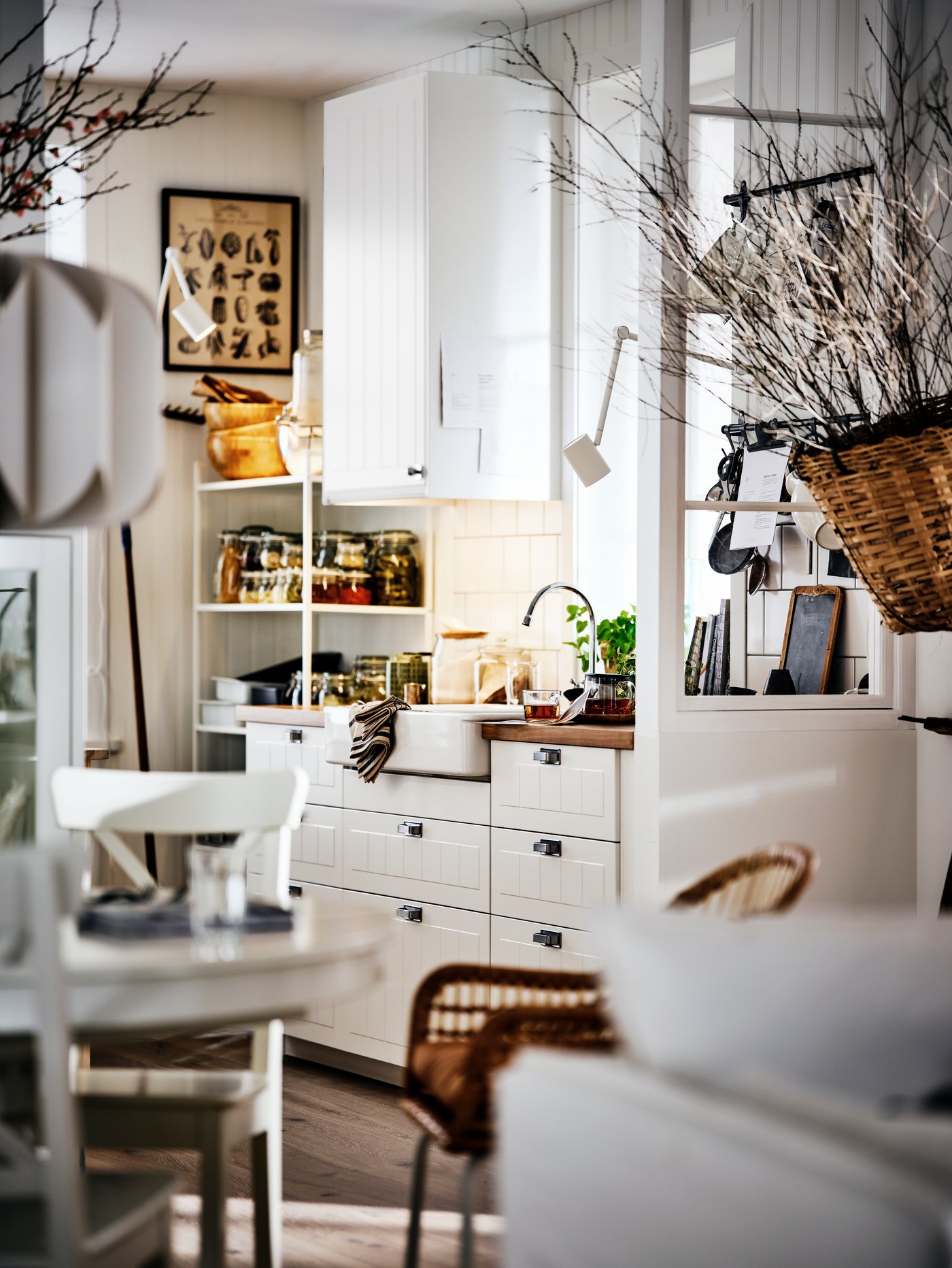 A white country-style kitchen and dining area, with white cabinets, a round table and decorative dried branches.