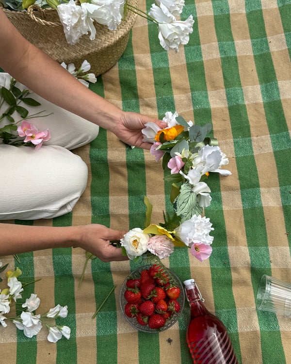 En person binder en enkel midsommarkrans med SMYCKA konstgjorda blommor.
