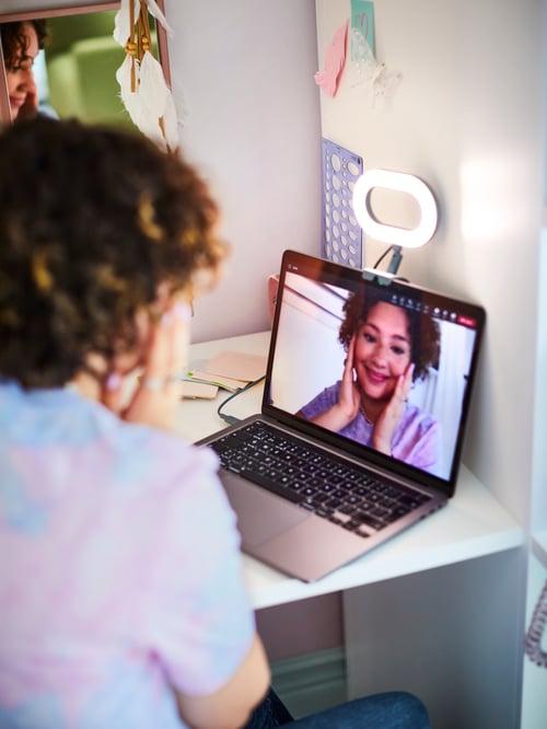O lampă inelară STÄNKREGN LED aprinsă este fixată deasupra unui laptop care se află pe un birou. Persoana se uită la ea pe laptop.