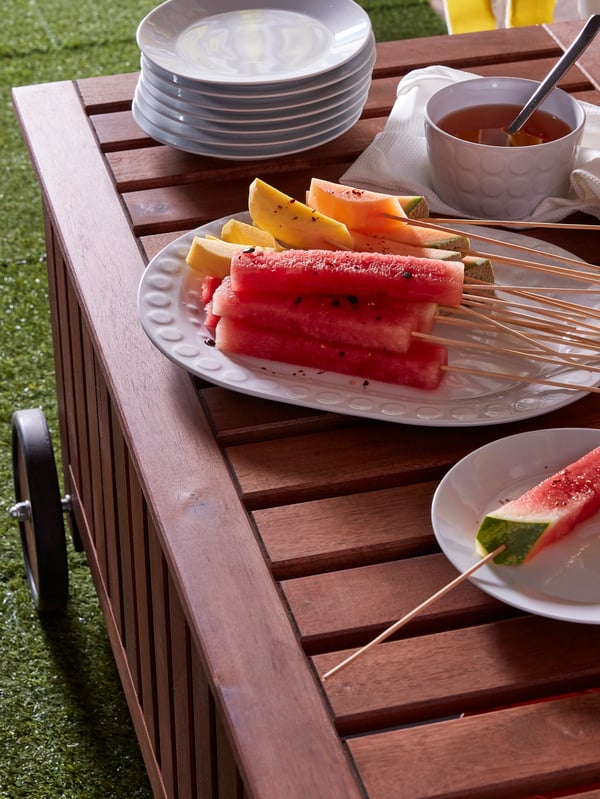 Platos IKEA 365+ con fruta sobre una mesa de madera ÄPPLARÖ en un espacio exterior.