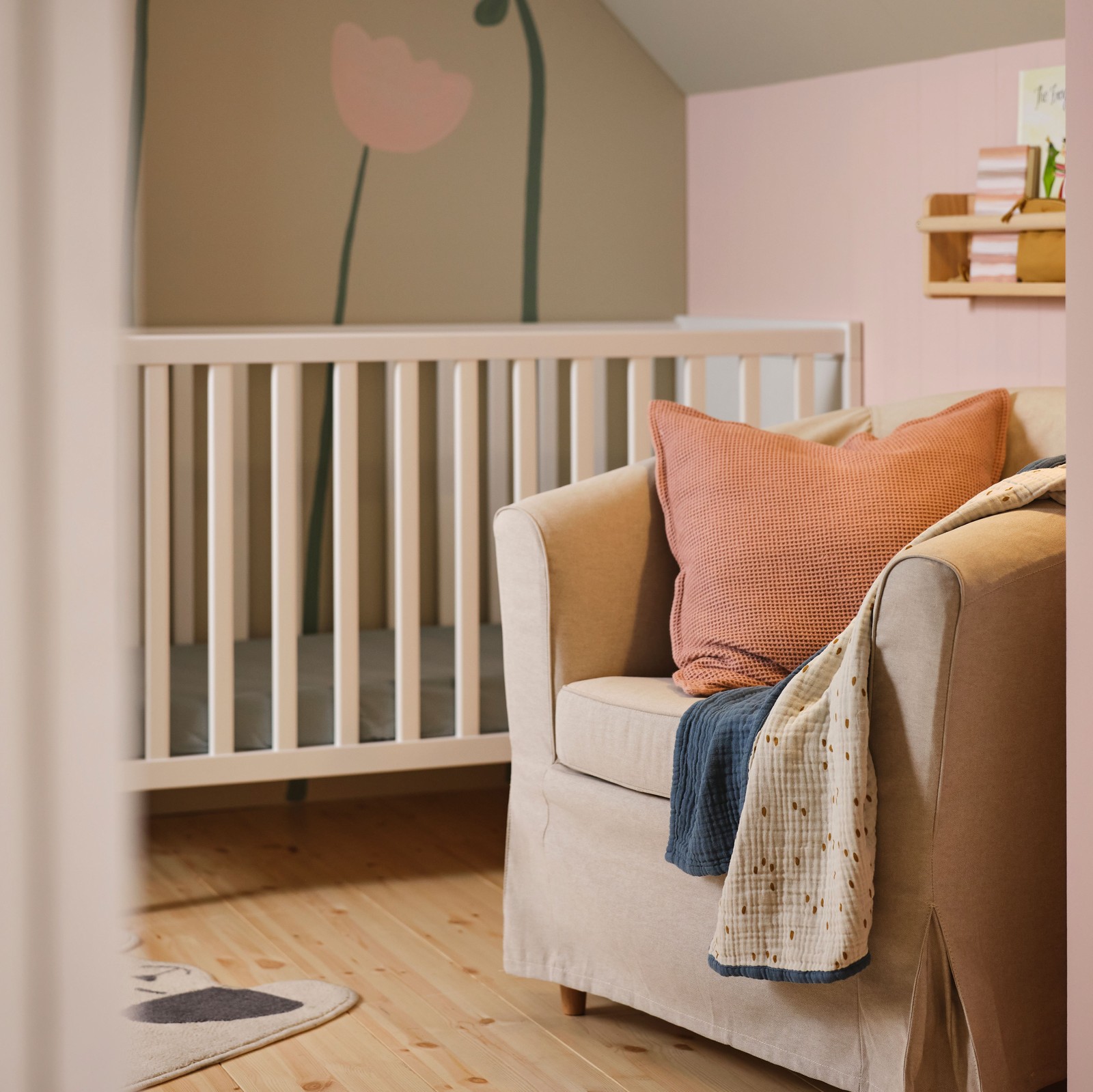 TULLSTA fotelja s Lofallet bež navlakom, na kojoj su GULDVÄVARE ćebe i jastučić u roze navlaci na fotelji, nalazi se pored SUNDVIK kreveca.